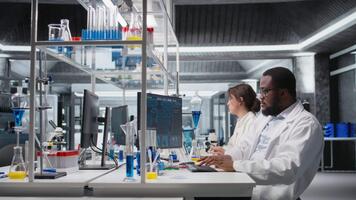 kvalitet kontrollera analytiker i labb testning blod prov använder sig av dator. afrikansk amerikan man i laboratorium analyserar sangvinisk vätska prov i injektionsflaska Begagnade för medicinsk forskning med pc programvara, kamera en video