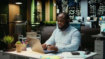 zwart kantoor werknemer controle een kennisgeving verbonden Aan socials terwijl hij doet na een tijdje Bij middernacht, controle smartphone Bij werk na uur. jong Mens lezing tekst berichten. camera a. video