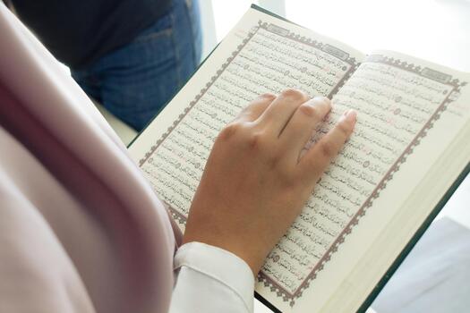 A person is reading a Quran with their hand on it. The book is open to a page with Arabic writing photo