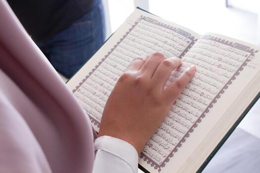 A person is reading a Quran with their hand on it. The book is open to a page with, Arabic writing photo