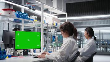 laboratorio técnico a escritorio mecanografía en verde pantalla ordenador personal teclado, mirando a molecular modelo, haciendo investigación tareas. mujer utilizando bioingeniería programa en Bosquejo computadora en médico laboratorio, cámara un video