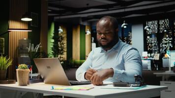 svart kille dokumentera grundläggande idéer på papper och läsning på bärbar dator, planera och schemaläggning uppgifter på natt. anteckna med hans handstil för en presentation den där speglar mål. kamera a. video
