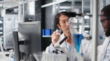 multietnisk nanoteknologi forskare använder sig av mikroskop till utvärdera cellulär strukturer i labb. olika arbetare konstaterar medicinsk vävnad genom förstoring verktyg på laboratorium bänk, kamera b video