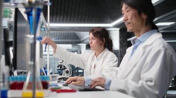 kemisk ingenjör använder sig av laboratorium glas med blå indikator lösning i forskning anläggningen. kemist ser på cylinder med kemisk vätska i labb, analyserar ämne egenskaper, kamera en video