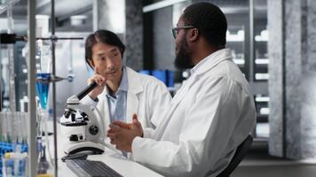 team av multietnisk forskare använder sig av mikroskop till utvärdera cellulär strukturer i labb. raser kollegor observera medicinsk vävnad genom förstoring verktyg på laboratorium bänk, kamera b video