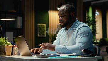 afrikansk amerikan kille granskning marknadsföra data och byggnad strategi för företag mål, använder sig av kalkylblad på bärbar dator för korrekturläsning. över tid efter timmar på multinationell företag. kamera b. video