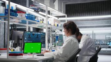 bioinformática científico trabajando en verde pantalla tableta en laboratorio, estudiando genómica información. mujer estudios adn hebra cartografía en croma llave dispositivo, contribuyendo a científico innovación, cámara un video