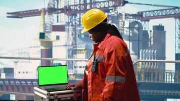 Green screen laptop used by drilling rig worker using handheld radio device to monitor systems. Offshore platform employee using walkie talkie, calibrating equipment with mockup notebook, camera B video
