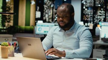 afrikansk amerikan kille svar e-postmeddelanden och dokumentera data från uppkopplad insikter för en multinationell företag, arbetssätt efter timmar i en mörk kontor. företag mål och utveckling. kamera b. video