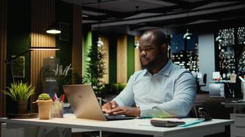 Black business consultant putting adhesive note on laptop screen as a memo, trying to remember a task from his to do list. Working late and leaving a reminder for next morning. Camera A. video