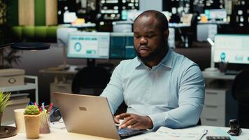 africano americano dipendente Lavorando a notte correzione di bozze ragnatela informazione, scrittura importante dati su il computer portatile. la creazione di un' sommario e progettazione strategia per allineare con impresa obiettivi. telecamera b. video