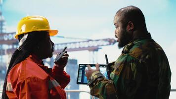 soldado en costa afuera plataforma cubierta hablando con técnico, utilizando dispositivo visualización software. africano americano naval unidad guardias perforación plataforma en contra terrorista amenazas utilizando tableta aplicación, cámara si video