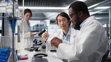 multietnisk nanoteknologi forskare använder sig av mikroskop till utvärdera cellulär strukturer i labb. olika arbetare konstaterar medicinsk vävnad genom förstoring verktyg på laboratorium bänk, kamera en video