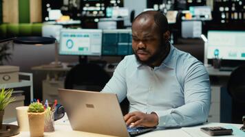 nero uomo d'affari afflitto e sovraccaricato dopo ore a scrivania, sperimentare posto di lavoro sfide e ansia. scoraggiato tipo lottando con intenso carico di lavoro e no gratuito volta. telecamera b. video