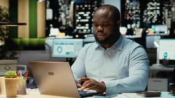 svart kontor anställd kontroll en underrättelse ansluten på socials medan han gör över tid på midnatt, kontroll smartphone på arbete efter timmar. ung man läsning text meddelanden. kamera b. video