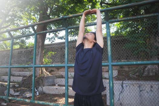 A man is stretching his arm in front of a fence. Concept of, determination and focus as the man works on his flexibility. photo