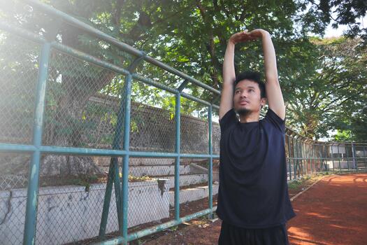 A man is stretching his arm in front of a fence. Concept of determination and focus as the man, works, on his flexibility photo