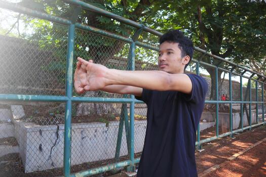 A man is stretching his arm in front of a fence. Concept of determination and, focus as the man, works on his flexibility, photo