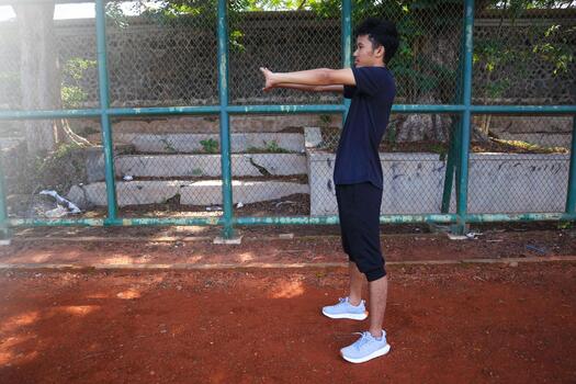 A man is stretching his arm in front of a fence. Concept of determination and, focus as the man works, on his flexibility photo