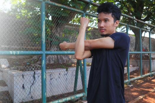 A man is stretching his arm in front of a fence. Concept of determination and focus as the, man works, on his flexibility photo