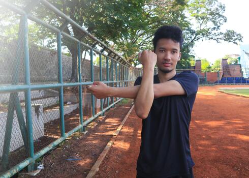 A man is stretching his arm in front of a fence. Concept of determination and focus, as the man works, on his flexibility photo
