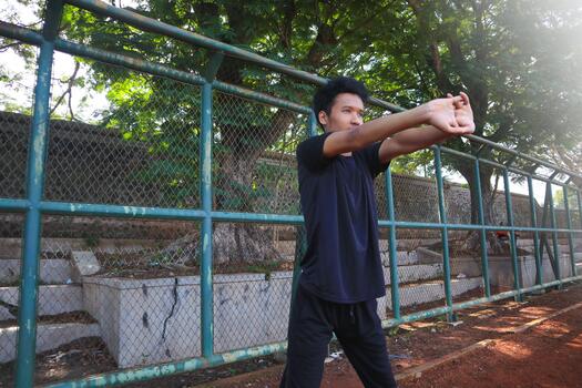 A man is stretching his arm in front of a fence. Concept of determination and focus as the man works on his, flexibility photo
