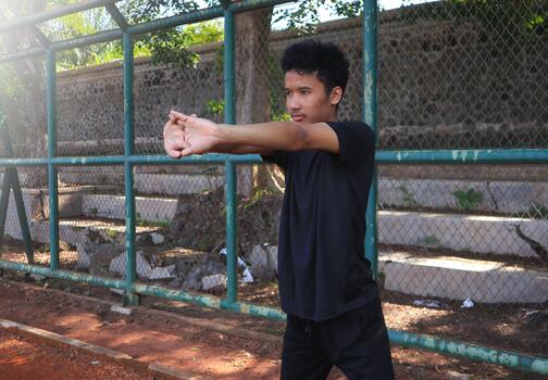 A man is stretching his arm in front of a fence. Concept of determination and focus as the man works on his, flexibility, photo