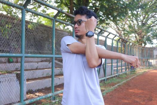 A man is stretching his arm in front of a fence. Concept of determination and, focus as the man works, on his flexibility, photo