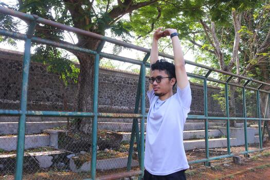 A man is stretching his arm in front of a fence. Concept of determination and, focus as the man works on his flexibility. photo