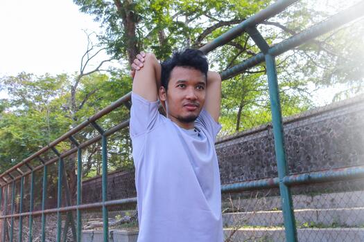 A man is stretching his arm in front of a fence. Concept of determination and focus as the man works, on his flexibility, photo