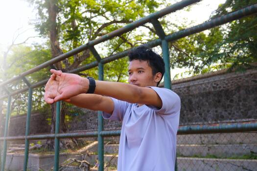 A man is stretching his arm in front of a fence. Concept of determination and focus as the man works on, his flexibility photo