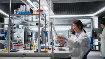 Scientist uses laboratory lamp to examine test subject in petri dish. Research facility technician holds medical container to light source, monitoring samples for impurity detection, camera A video