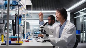 clinique microbiologiste examiner microscope verre faire glisser dans laboratoire à vue cellules. asiatique laboratoire ouvrier chèques échantillon faire glisser avant imagerie processus en utilisant optique appareil, caméra une video