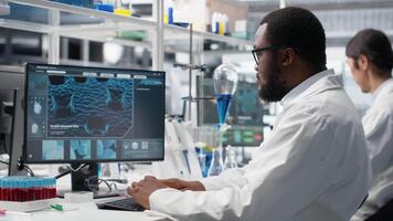 molecular biólogo usos computadora programa mostrando adn datos, quitando los anteojos. africano americano hombre confuso por bioinformática genómica software análisis en ordenador personal en laboratorio, cámara si video