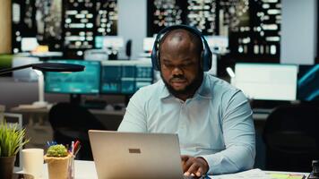 negro persona gerente diario Tareas después horas con atención música en auriculares, hallazgo inspiración con ambiente sonidos a ayuda con concentración y productividad. masculino trabajador multitarea cámara b. video