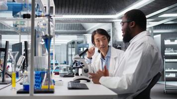 team av multietnisk forskare använder sig av mikroskop till utvärdera cellulär strukturer i labb. raser kollegor observera medicinsk vävnad genom förstoring verktyg på laboratorium bänk, kamera en video