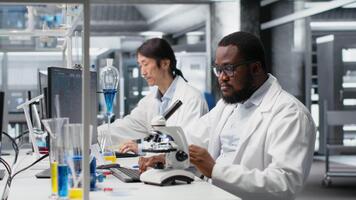 clinique microbiologiste en fonctionnement composé microscope Est-ce que détaillé échantillon observation, enregistrement résultats. biotechnologie expert études tissu en dessous de optique appareil, documenter résultats, caméra b video