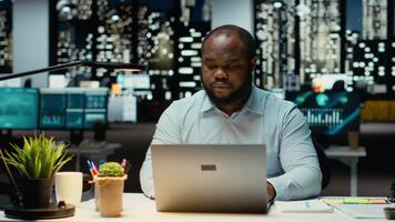 svart företag konsult arbetssätt efter timmar faktum kontroll webb information, skrivning Viktig data på bärbar dator. skapande en sammanfattning och design strategi till justera med företag mål. kamera b. video