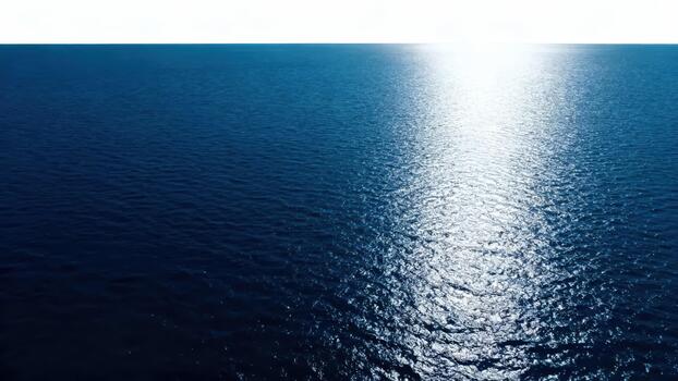 Bright sunlight reflects intensely across the deep blue ocean surface extending to the horizon photo