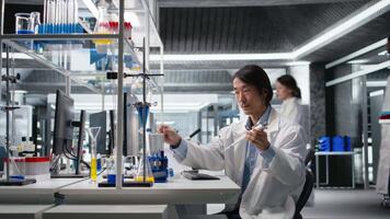 laboratorio ingegnere fa pipettaggio procedura con chimico reagente, miscelazione soluzioni per reazione test. anziano scienziato usi pipetta per trasferimento liquido in test tubo, tremante per miscela, telecamera un' video