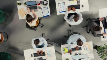 top naar beneden visie zoom in van bedrijf mensen recensie diagrammen gedurende verslag doen van schrijven. collega's in multinational bedrijf delen inzichten en coördineren taken gebruik makend van pc en zichtbaar gegevens hulpmiddelen. camera a. video