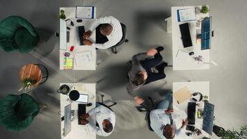 Top down view zoom in of workers in multinational company discuss business strategy and performance metrics. Staff consult on forecasting, report sharing and data while aligning objectives. Camera A. video