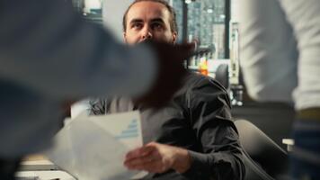 o negócio pessoas discutir desenvolvimento estratégias e analytics usando documentos. profissional empregados Reveja documentação, previsões, e intuições para realçar corporativo planejamento. Câmera b. video