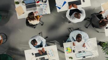 Top down view zoom in of employees engaged in business intel and analytics using data diagrams in office, staff reviews projections and reports to improve overall company strategy. Camera A. video