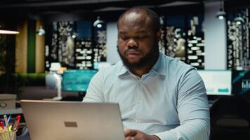 Black employee engages in methodical planning at night in corporate workspace, projecting new ideas and reflecting on business outlooks to find solutions for a challenging problem. Camera A. video