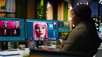 negro foto editor trabajando con retocar software a virtual asistente, computadora corriendo avanzado diseño programa y ai en doble monitores artístico digital medios de comunicación en moderno creativo oficina. cámara b. video