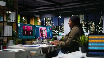 negro foto editor trabajando con retocar software a virtual asistente, computadora corriendo avanzado diseño programa y ai en doble monitores artístico digital medios de comunicación en moderno creativo oficina. cámara una. video