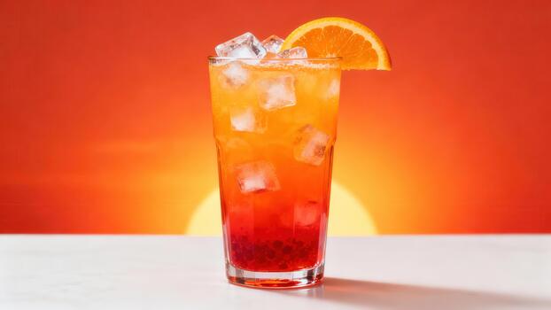 Tall glass containing a layered tropical beverage with ice cubes and citrus garnish sits against a vibrant sunset background photo