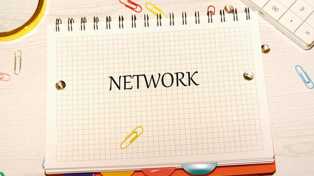 The word NETWORK is written on a white notepad with a grid pattern. The notepad is surrounded by paper clips, push pins, and a calculator on a bright white desk photo