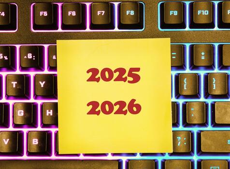 A yellow sticky note with 2025 and 2026 written on it sits on top of a colorful, modern computer keyboard with illuminated keys. Thinking about future planning photo
